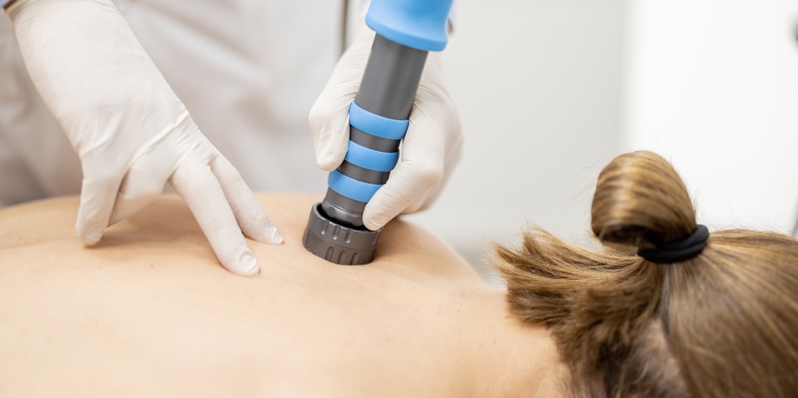 Doctor applies shock wave therapy with special medical equipment on men's back at medical office, close-up view. Concept of non-invasive technology for treating pain in the musculoskeletal system