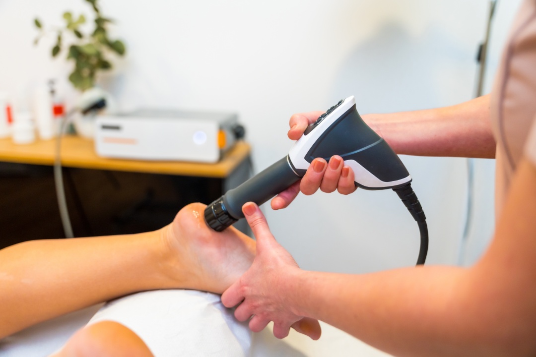 Close-up of an unrecognizable patient on stretcher receiving a shockwave therapy massage on foot in a holistic clinic