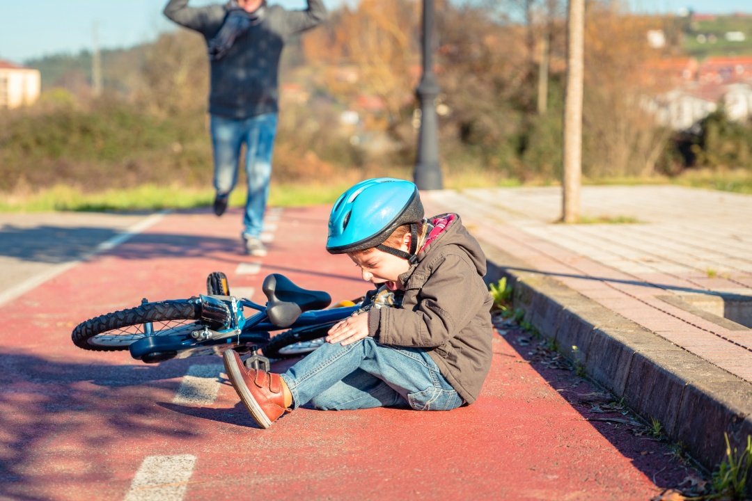 Boy in the street ground with a knee injury screaming after falling off to his bicycle