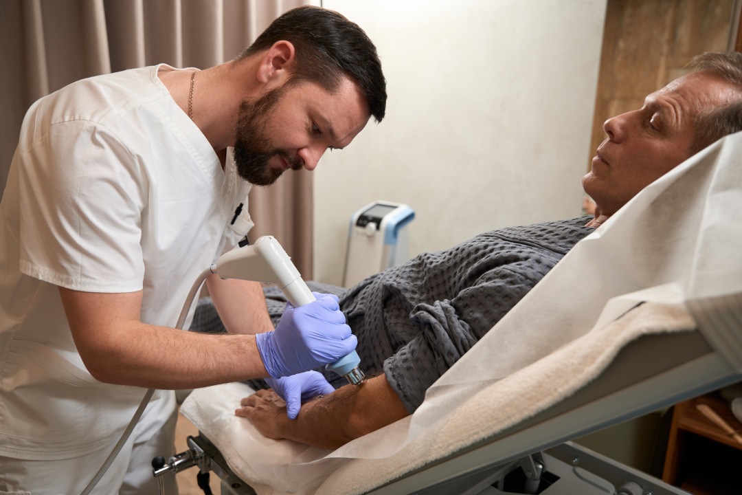 Calm man on hospital bed having his arm treated with shockwave therapy